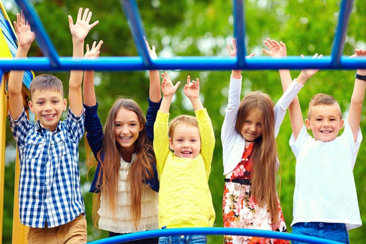 Cheerful children posing at the playground together and hands up